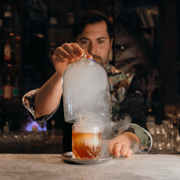 Giacomo Giannotti lifting the glass cover of the Great Gatsy, an Old-Fashioned style cocktail from Paradiso, which uses smoke.